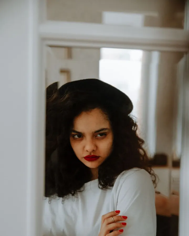 A woman with curly hair looking thoughtfully into a mirror
