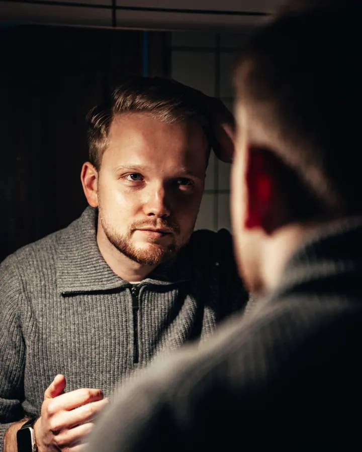 A man studying his hairline in a mirror